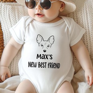 May include: White baby onesie with a black dog face graphic and the text "Max's New Best Friend". The baby is wearing sunglasses and a straw hat. The onesie is short-sleeved.