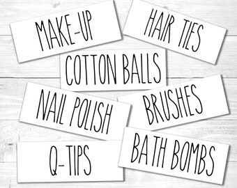 May include: White labels with black text for bathroom organization. The labels read: "MAKE-UP", "HAIR TIES", "COTTON BALLS", "NAIL POLISH", "BRUSHES", "BATH BOMBS", and "Q-TIPS".