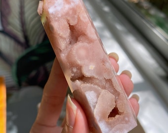 May include: A pink and white agate crystal point with a unique, natural, druzy formation. The crystal is translucent and has a smooth, polished surface.