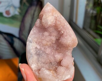 Puede incluir: Un cúmulo de cristal de amatista rosa y blanco con una punta puntiaguda y una superficie rugosa y texturizada.