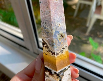 May include: A multi-colored crystal point with pink, white, yellow, and brown bands. The crystal is polished and has a pointed tip.