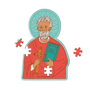 May include: A red and blue jigsaw puzzle piece featuring a saint holding a book with the words "Holy Bible" on the cover. The saint is holding a cross in his other hand. The puzzle piece is labeled "St. Valentine".