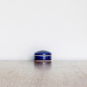 May include: A small, round, blue ceramic trinket box with a white rim.