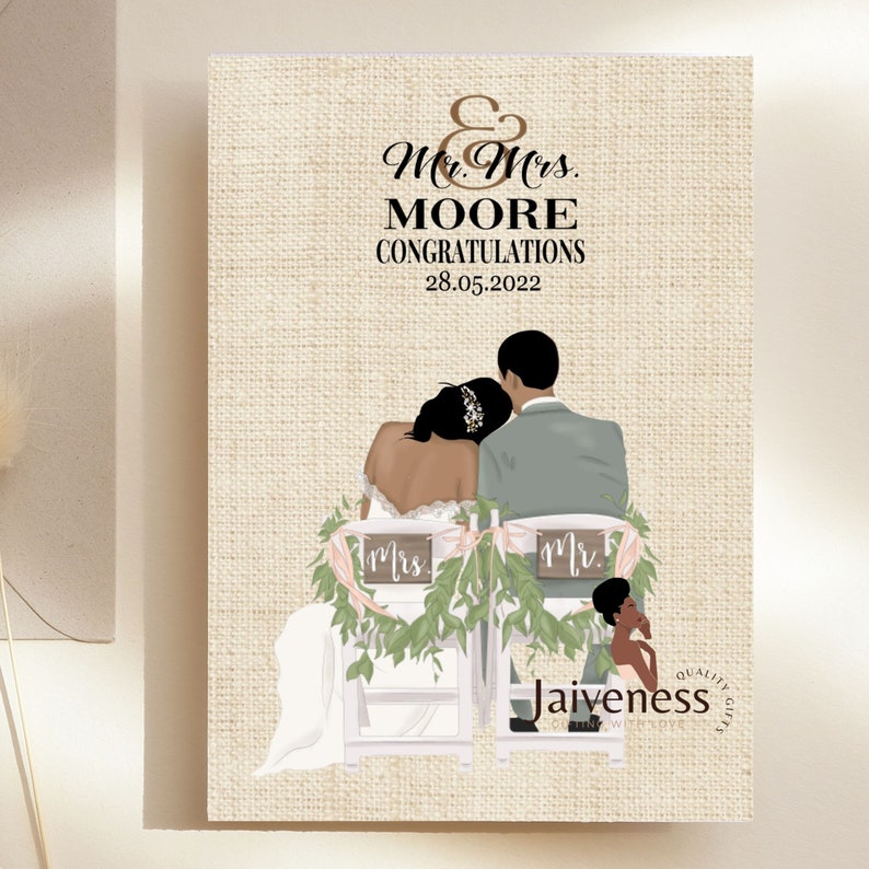 Peut inclure: Une carte de mariage avec un fond en toile de jute repr&eacute;sentant une illustration de dessin anim&eacute; d'un couple noir assis sur des chaises avec de la verdure et des pancartes indiquant "Mr." et "Mrs.". Le texte sur la carte est "Mr. & Mrs. MOORE CONGRATULATIONS 28.05.2022" et "Jaivness Quality Gifts".