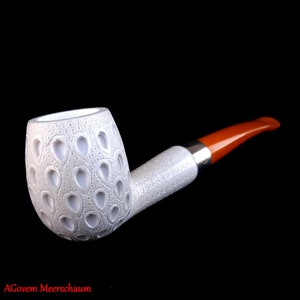 Puede incluir: Una pipa de espuma de mar blanca con un diseño estampado y una boquilla naranja.