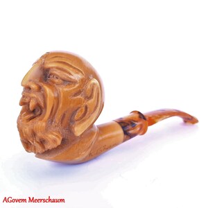 May include: A brown meerschaum pipe with a carved human face on the bowl. The pipe is signed "H. Gauen".