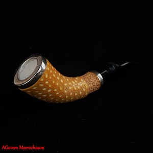 May include: A curved meerschaum pipe with a silver band and a black stem. The bowl of the pipe is a light brown color and has a textured surface.