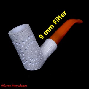 Puede incluir: Pipa de espuma de mar blanca con un diseño intrincado y un filtro naranja de 9 mm. La pipa está hecha de un material blanco y tiene una cazoleta redonda. El filtro está hecho de un material naranja y está unido a la pipa.