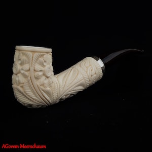 May include: A white meerschaum pipe with intricate floral carvings. The pipe has a black ebonite stem and a silver band.
