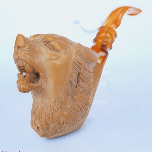 May include: A brown wooden pipe with a wolf head design. The pipe has a brown stem and a brown bowl. The wolf's mouth is open and its teeth are visible.