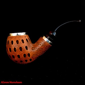 May include: A brown meerschaum pipe with a silver band and a carved design. The pipe has a long, curved stem.