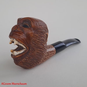 Puede incluir: Una pipa de espuma de mar marrón con una cabeza de mono tallada y una boquilla negra. La pipa está firmada "A. Goven".