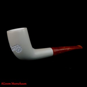 Puede incluir: Una pipa de espuma de mar blanca con una boquilla roja. La cazoleta de la pipa tiene un diseño decorativo.