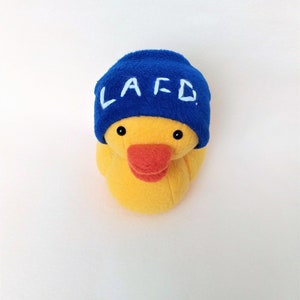 May include: A yellow rubber duck wearing a blue hat with the letters "LAFD" embroidered in white.