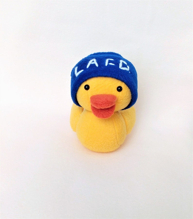 May include: A yellow plush duck wearing a blue hat with the letters "LAFD" embroidered in white.