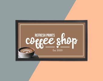 May include: A brown framed sign with white text that reads "REFRESH PRINTS coffee shop Est. 2020". A cup of coffee with latte art is in the bottom left corner of the sign.