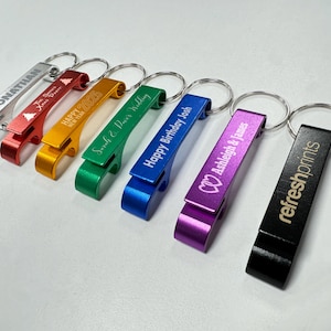 May include: Seven different coloured bottle openers with key rings. The bottle openers are engraved with personalised messages, including names, dates, and a happy birthday message. The bottle openers are silver, red, gold, green, blue, purple, and black.