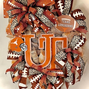 May include: A decorative wreath featuring the Texas Longhorns logo. The wreath is adorned with orange and brown ribbons, football-themed accents, and a large "UT" in the center. The design includes a football and a helmet.