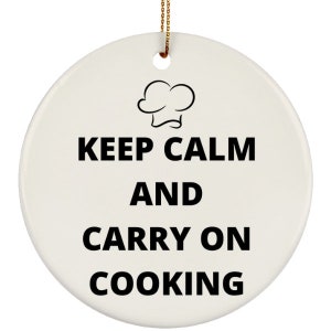 May include: White ceramic Christmas ornament with a black chef's hat and the text "Keep Calm and Carry On Cooking".