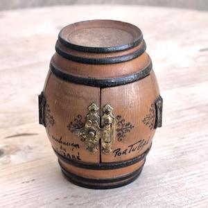 Könnte beinhalten: Kleine, fassförmige Holzkiste mit Klapptür und Metallverschluss. Die Kiste ist braun mit schwarzen Bändern und dekorativen Akzenten. Der Text "Portugal" ist auf der Seite sichtbar.