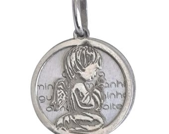 May include: A circular silver-coloured pendant featuring a raised relief of a kneeling angel with hands clasped in prayer. The background of the pendant displays engraved text in a light font, and the piece includes a small silver-coloured bail at the top.