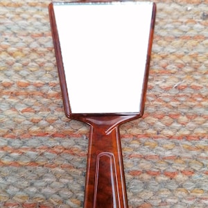 May include: A brown plastic hand mirror with a rectangular mirror surface.