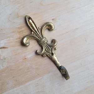 Peut inclure: Un crochet en métal doré en forme de fleur de lys. Le crochet est conçu pour accrocher des objets au mur.