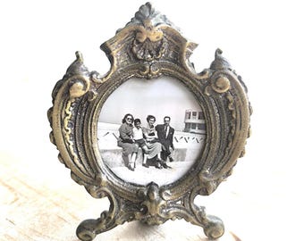 Puede incluir: Marco de fotos ornamentado de estilo antiguo con una abertura circular. El marco es de metal dorado y presenta intrincados adornos y una cresta decorativa. Contiene una fotografía en blanco y negro de una familia.