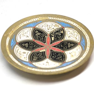 May include: An oval, decorative dish with a gold-colored rim. The center features a floral design in black, white, red, and blue. The dish has a detailed, ornate pattern.