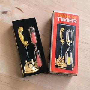 May include: A black box with a gold telephone hourglass timer inside. The box has the words "Telephone Timer" printed on it in white letters.