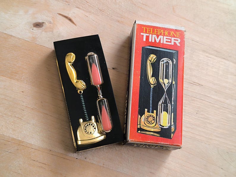 May include: A black box with a gold telephone hourglass timer inside. The box has the words "Telephone Timer" printed on it in white letters.