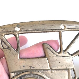 May include: Vintage brass train-shaped wall decor. The decorative piece features a detailed design of a train engine with cut-out windows and a circular front. The brass has a weathered appearance, suggesting age and use.