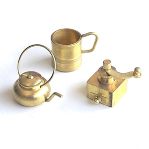 May include: Miniature brass kitchenware set comprising a small kettle, a mug, and a coffee grinder. The items are presented on a white background, highlighting their intricate design and golden hue, perfect for a dollhouse.