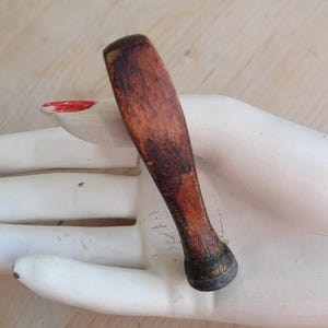Könnte beinhalten: Ein Holzstift mit abgerundetem Ende. Der Stift ist braun mit einer dunkelbraunen Beize. Der Stift ist etwa 7,5 cm lang.