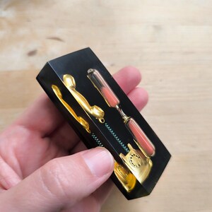 May include: A black resin paperweight with a gold rotary phone and an hourglass with pink sand. The phone and hourglass are embedded in the resin.