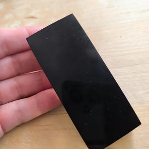 May include: A black rectangular piece of polished obsidian, a type of volcanic glass, with a smooth, shiny surface.