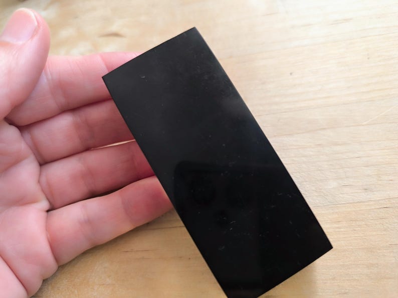 May include: A black rectangular piece of polished obsidian, a type of volcanic glass, with a smooth, shiny surface.
