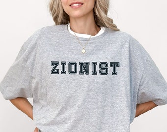Op de afbeelding: Een lichtgrijs oversized T-shirt met het woord "ZIONIST" in donkerblauwe blokletters. Het shirt heeft een ronde hals en korte mouwen. Het model draagt een zwarte short.