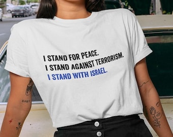May include: White t-shirt with the text "I STAND FOR PEACE. I STAND AGAINST TERRORISM. I STAND WITH ISRAEL." in black and blue. The shirt is worn by a person wearing a black cap and black skirt.