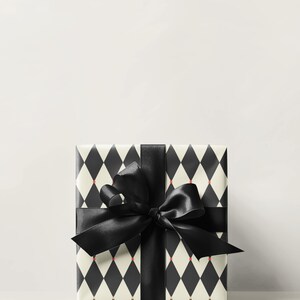 May include: A wrapped gift box featuring a black and white harlequin pattern with small red accents. The box is tied with a wide black satin ribbon and bow, creating a classic and elegant presentation.