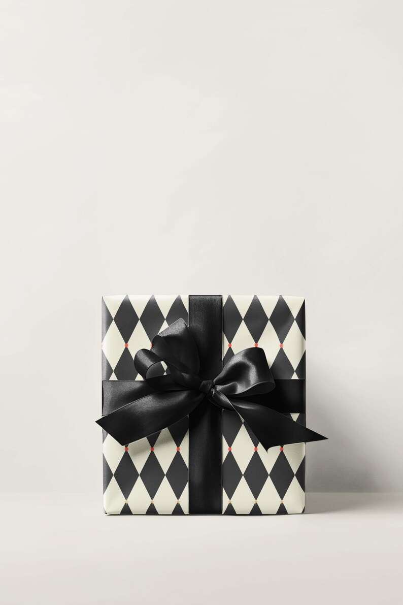 May include: A wrapped gift box featuring a black and white harlequin pattern with small red accents. The box is tied with a wide black satin ribbon and bow, creating a classic and elegant presentation.