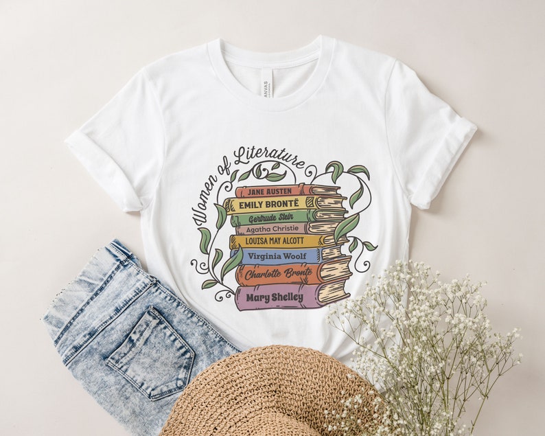 May include: White t-shirt with a graphic of a stack of books with the names of famous female authors, including Jane Austen, Emily Bronte, Agatha Christie, and Louisa May Alcott. The text "Women of Literature" is above the books.