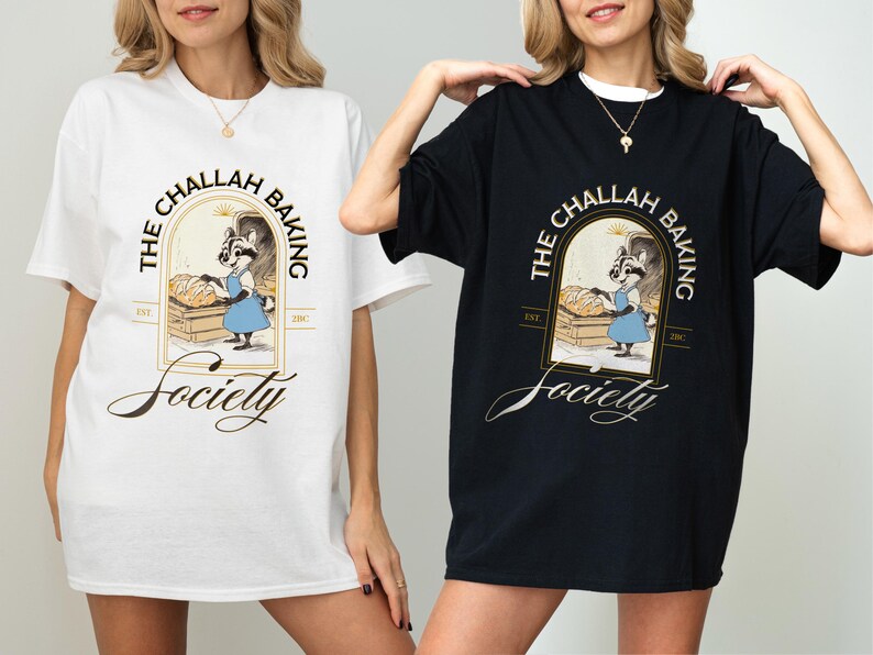 K&ouml;nnte beinhalten: Wei&szlig;e und schwarze T-Shirts mit dem Text "THE CHALLAH BAKING Society" und einer Illustration eines B&auml;ckerracoon. Das Design befindet sich in einem goldenen Rahmen mit den Worten "EST. 2017". Die Shirts sind kurz&auml;rmelig und haben eine lockere Passform.