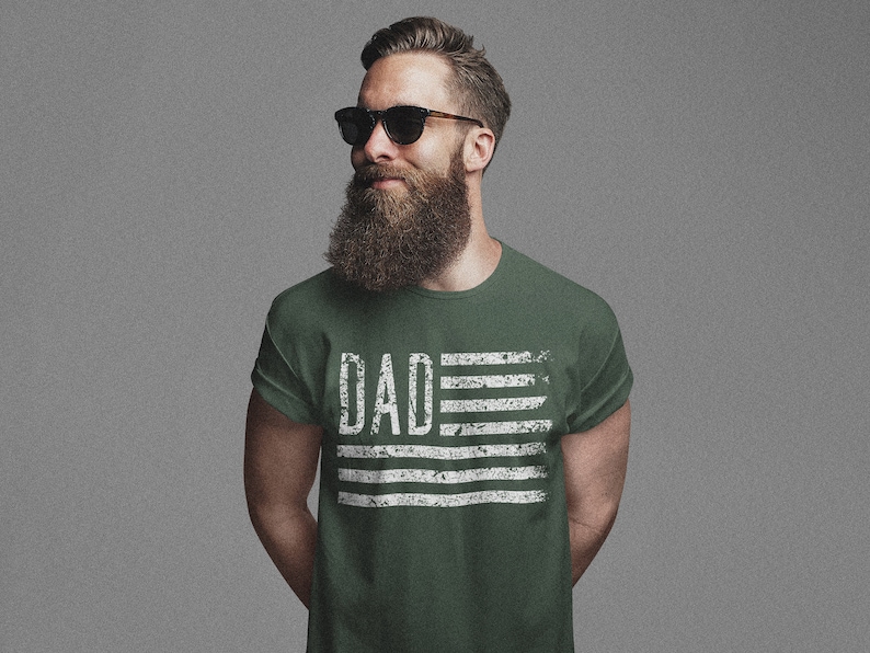 May include: A green t-shirt with a white distressed American flag design and the word "DAD" printed on it.