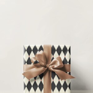 May include: A wrapped gift box with a brown satin ribbon and bow. The wrapping paper has a black and white diamond pattern with small red accents. The gift is presented on a white background.