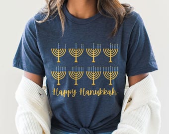 May include: A navy blue t-shirt with a graphic of nine gold menorahs with blue flames. The text "Happy Hanukkah" is printed below the menorahs.