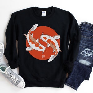 May include: Black sweatshirt featuring a design of two koi fish in a circle against a red background. The fish are white and orange, with Japanese characters below. The sweatshirt is paired with blue jeans and gray sneakers.