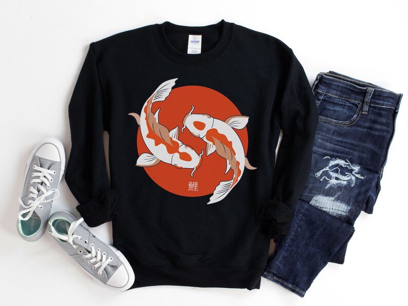 May include: Black sweatshirt featuring a design of two koi fish in a circle against a red background. The fish are white and orange, with Japanese characters below. The sweatshirt is paired with blue jeans and gray sneakers.