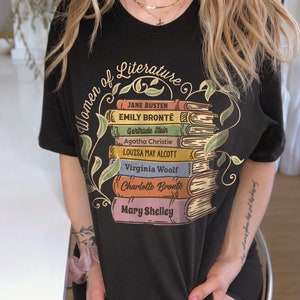 May include: Black t-shirt with a graphic of a stack of books featuring the names of famous women of literature, including Jane Austen, Emily Bront&euml;, Gertrude Stein, Agatha Christie, Louisa May Alcott, Virginia Woolf, Charlotte Bront&euml;, and Mary Shelley.