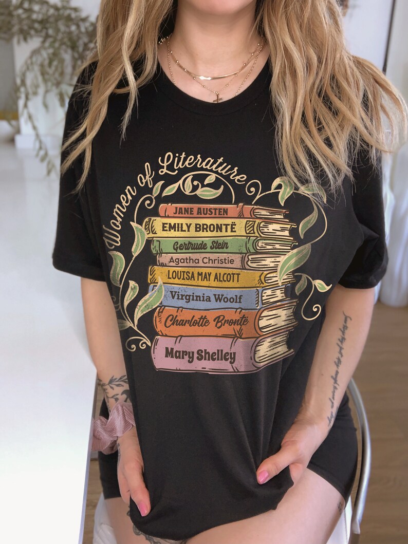 May include: Black t-shirt with a graphic of a stack of books featuring the names of famous women of literature, including Jane Austen, Emily Bront&euml;, Gertrude Stein, Agatha Christie, Louisa May Alcott, Virginia Woolf, Charlotte Bront&euml;, and Mary Shelley.